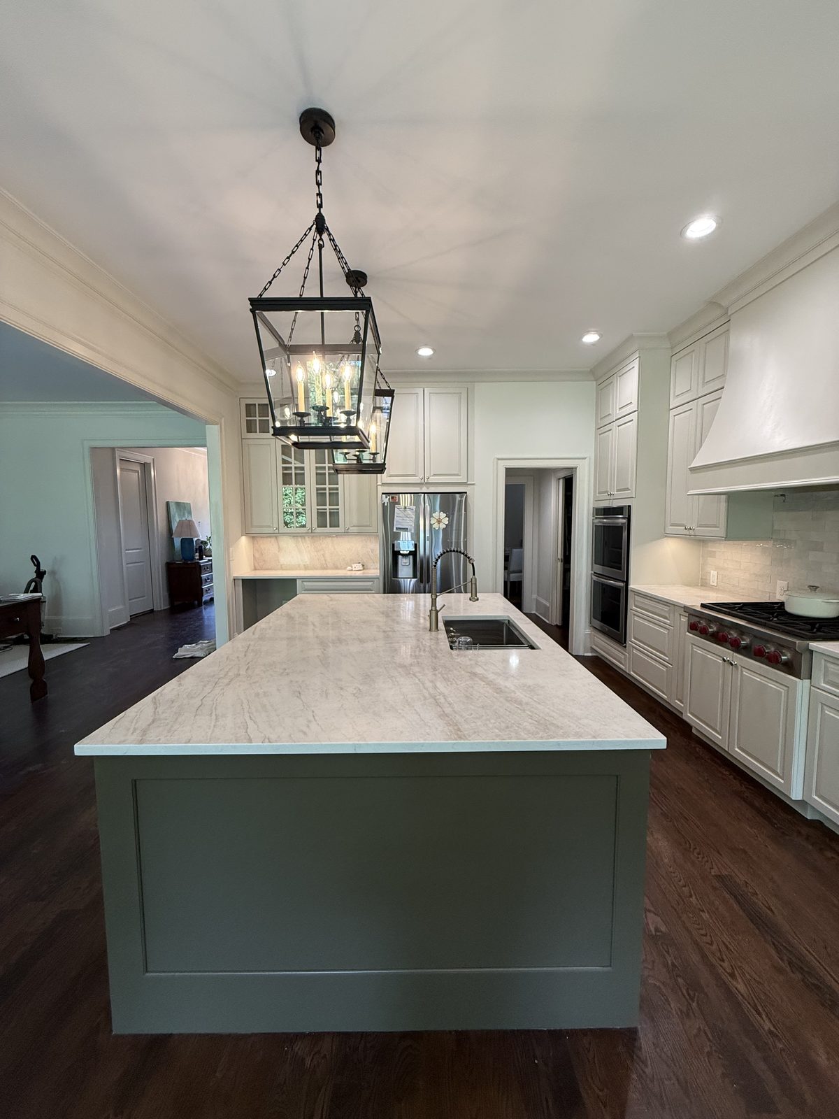 Long sage green kitchen island with a marble countertop beneath iron lantern pendants — Lou's Atlanta Painting