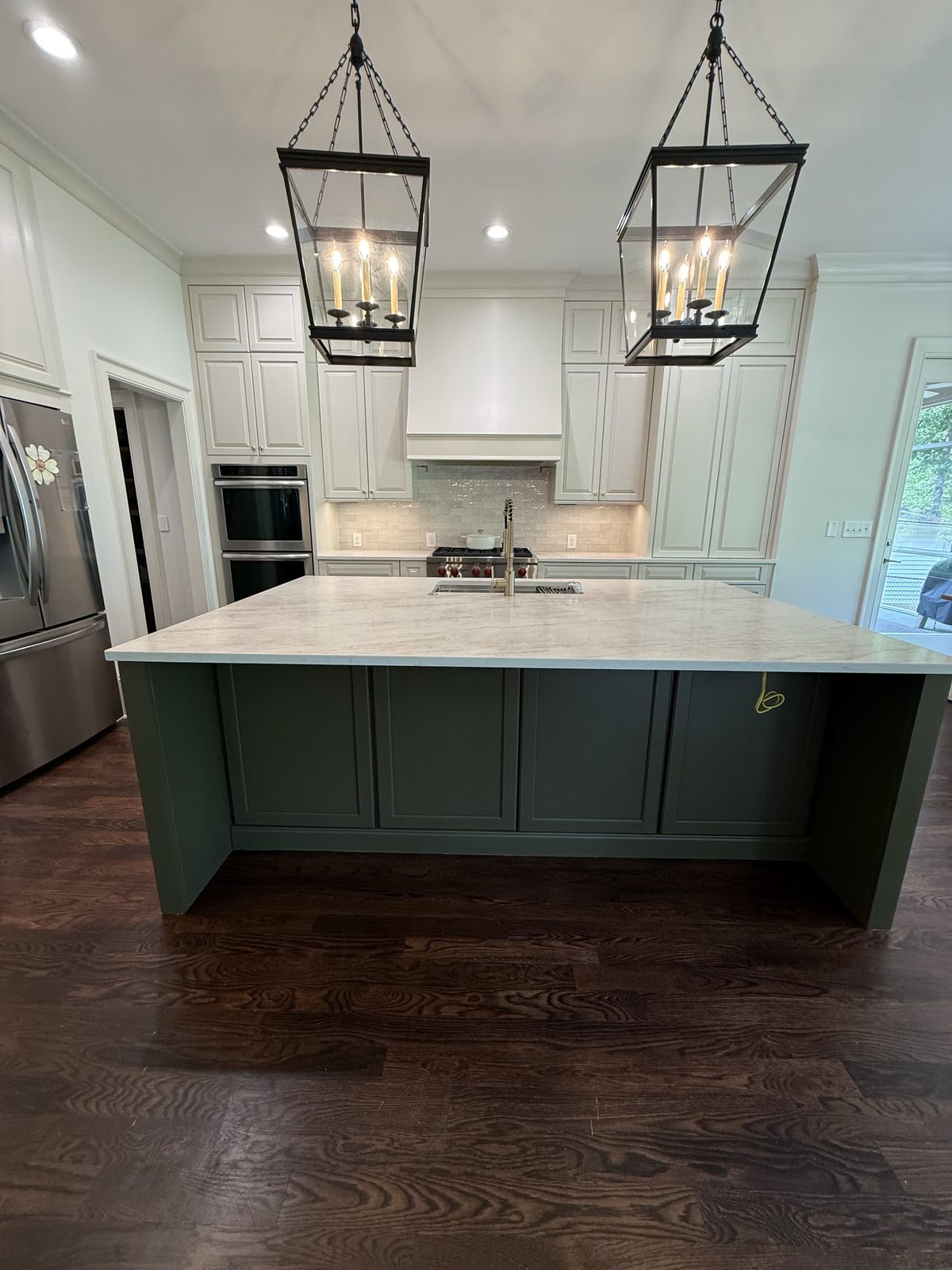 Sage green kitchen island and off-white cabinetry beneath a white plaster range hood — Lou's Atlanta Painting