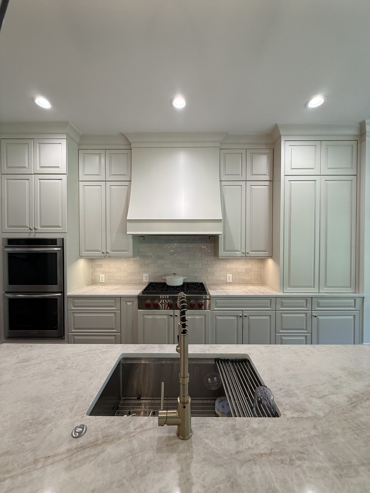 Kitchen range wall with a tile backsplash, white hood, and refinished cabinets in soft greige — Lou's Atlanta Painting